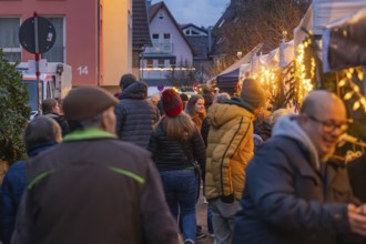 People stroll through an illuminated night market in a street, Aidlingen Christmas market,
