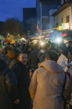 Large crowd enjoying the night atmosphere at a busy Christmas market with stalls and lights,