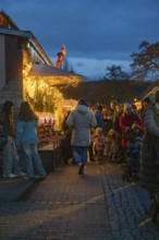 People stroll along illuminated market stalls at dusk, Aidlingen Christmas market, Böblingen