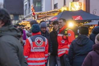 Red Cross members in uniforms happily interact at a well-attended Christmas market, Aidlingen