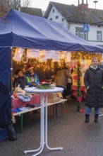 People stand at a decorated market stand under a tent at a busy Christmas market, Aidlingen