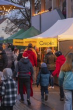 Visitors stroll along illuminated stands at an evening market, Aidlingen Christmas Market,