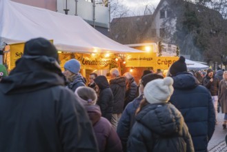 People wearing winter clothes in front of illuminated food stalls at a market, Aidlingen Christmas