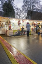 A market stall at dusk with people looking at goods while it rains, Aidlingen Christmas market,