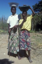 Two local woman balance bowls on their heads and pose for the camera at Kande on Lake Malawi,