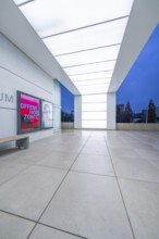 Modern museum entrance with blue lighting and large windows in the evening, Open Horizons