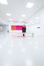White minimalistic room with woman on a bench in front of colored painting, Open Horizons