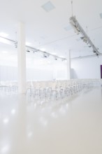 Minimalistic hall with rows of white chairs and bright light sources, Open Horizons exhibition,
