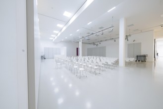 Large, empty hall with lots of white chairs in a minimalistic, bright setting, Open Horizons