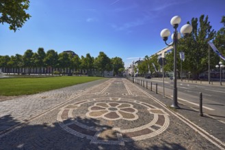 Paving stone sidewalk, mosaic, pattern, barrier bollard, lantern, trees, flags on flagpoles,