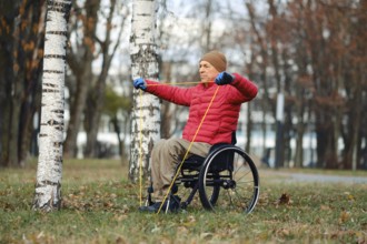 A man in a red jacket and beige hat performs strength training using resistance bands while seated
