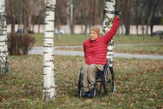 A person in a wheelchair stretches one arm up under the clear sky in a peaceful park filled with