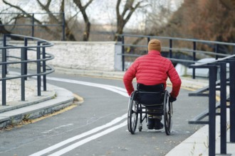 Active person in a red jacket uses a wheelchair to move along a winding path