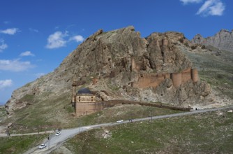 A mountain fortress with roads in the foreground surrounded by steep rocks under a bright blue sky,