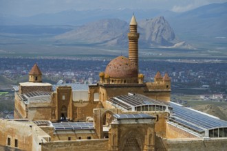 An ancient dome mosque in a mountainous landscape surrounded by a city under a blue sky, Ishak