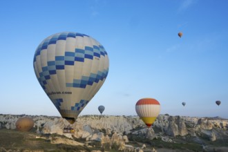 Hot air balloons of various colors float over a picturesque landscape and stand out against the