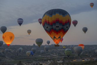 Colourfully patterned hot air balloons rise over the city and countryside of Cappadocia, Göreme