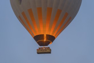 Close-up of glowing hot air balloon with basket and flame against the morning sky, Göreme Tarihî