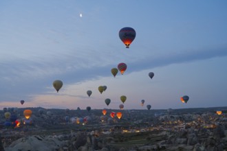 Many hot air balloons float at dusk over the picturesque landscape of Cappadocia, Göreme National