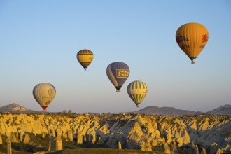 Different colored balloons float over a rocky landscape in golden light, hot air balloons, Göreme