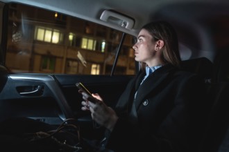 Woman traveling as a passenger in a ride hailing car at night, looking out the window while holding