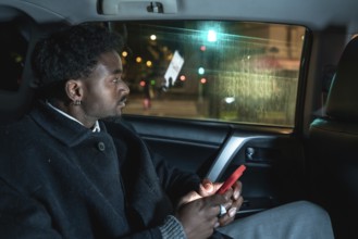 Afro american passenger riding in a car, looking out the window at city lights while holding a