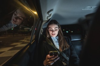 Young businesswoman in backseat at night, focused on smartphone screen while commuting through