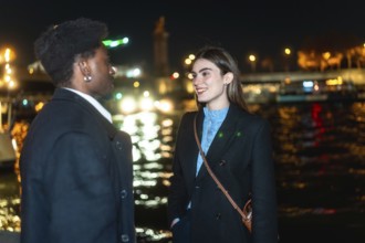 Young diverse couple standing by paris river at night, enjoying an intimate conversation during a