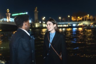 Young couple enjoying a romantic conversation by the illuminated river at night, sharing an