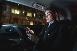 Young businesswoman commuting by car at night, focused on her smartphone as she scrolls messages