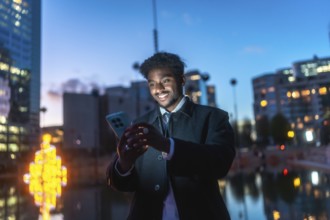 African american man smiling while engaging with a smartphone, viewing content under the