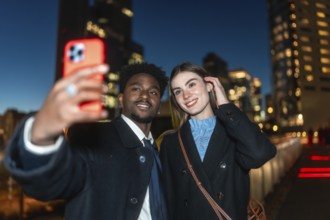 Diverse couple happily capturing a moment together using a mobile device for a selfie, illuminated