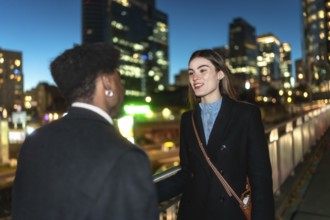Two colleagues converse warmly on an urban pedestrian bridge at night, city lights and blurred