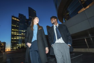 Diverse business colleagues walking down a city street at night, smiling and laughing together with