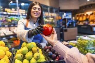 Greengrocer providing customer with a fresh organic tomato, emphasizing quality service and healthy