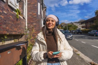 Young woman walking confidently down a sunny city street in autumn, smiling and enjoying music on
