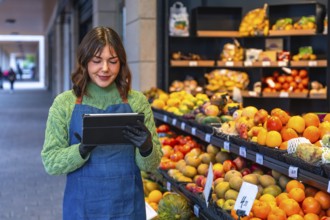Female small business owner wearing an apron and gloves managing stock and orders on a digital