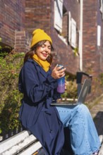Young woman sitting on a park bench in an urban environment, using her laptop for digital nomad
