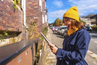 Young smiling woman wearing a yellow beanie and blue trench coat showing excitement finding a