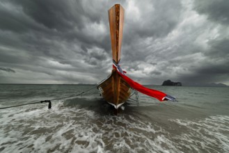 Longtail boat on the beach with dark rain clouds behind it, Koh Ngai island, Andaman Sea, Satun
