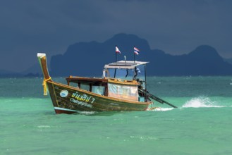 Longtail boat in fast drive to the beach, behind it an approaching thunderstorm, Koh Ngai island,