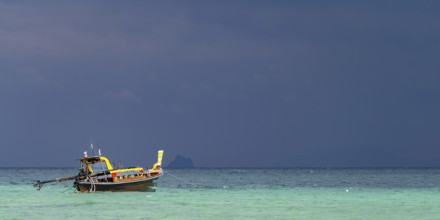 Longtail boat (Thai: Ruea Hang Yao) on the beach, behind it an approaching thunderstorm, Koh Ngai