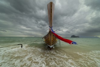 Longtail boat on the beach with dark rain clouds behind it, Koh Ngai island, Andaman Sea, Satun