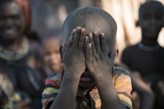 Himba child holding hands in front of face, traditional Himba village, Kaokoveld, Kunene, Namibia
