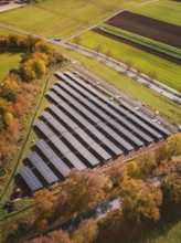Solar field in autumn surroundings, surrounded by colorful trees and fields, from a bird's eye