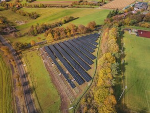 Aerial view of a solar field in an autumn landscape with fields and colorful trees, PV