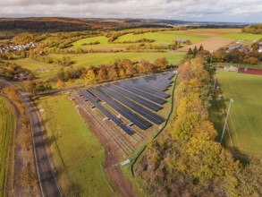 Large solar field in an autumn landscape, surrounded by green fields and trees, Bau PV