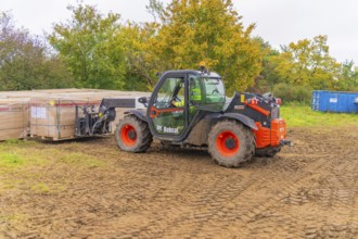 A forklift truck transports boxes across muddy soil in an autumn environment, Bau PV