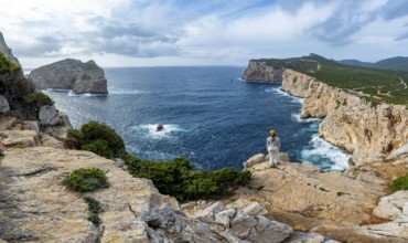 Tourist enjoying the view of steep cliffs by the sea and the rocky island of Isola Foradada, cliffs