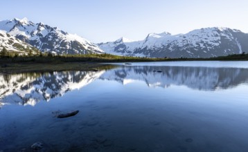 Mountain peaks with Portage Glacier glacier and snow reflected in Divide Lake mountain lake in